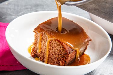 Side view of pouring caramel on sticky toffee pudding