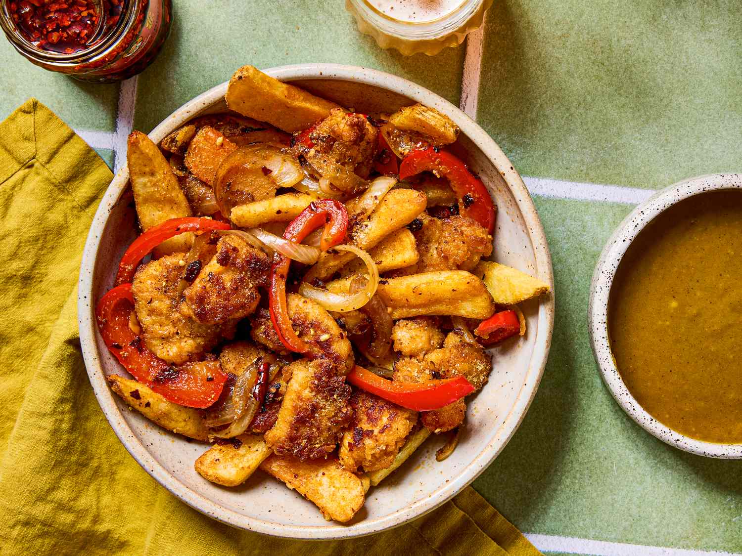 A bowl with fried food including vegetables and meats served with sauces on a table