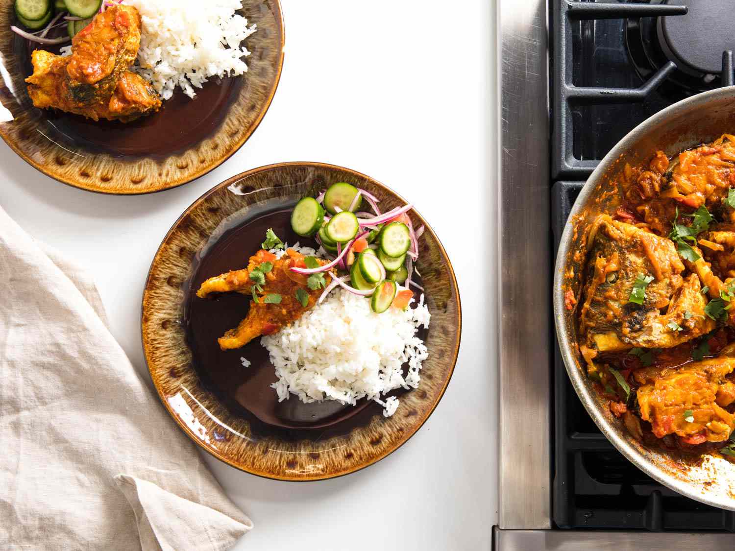 A top-down shot of two plates of fish bhuna with rice and cucumber salad.