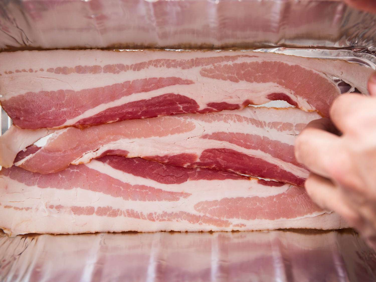 An aluminum loaf pan is lined with strips of bacon.