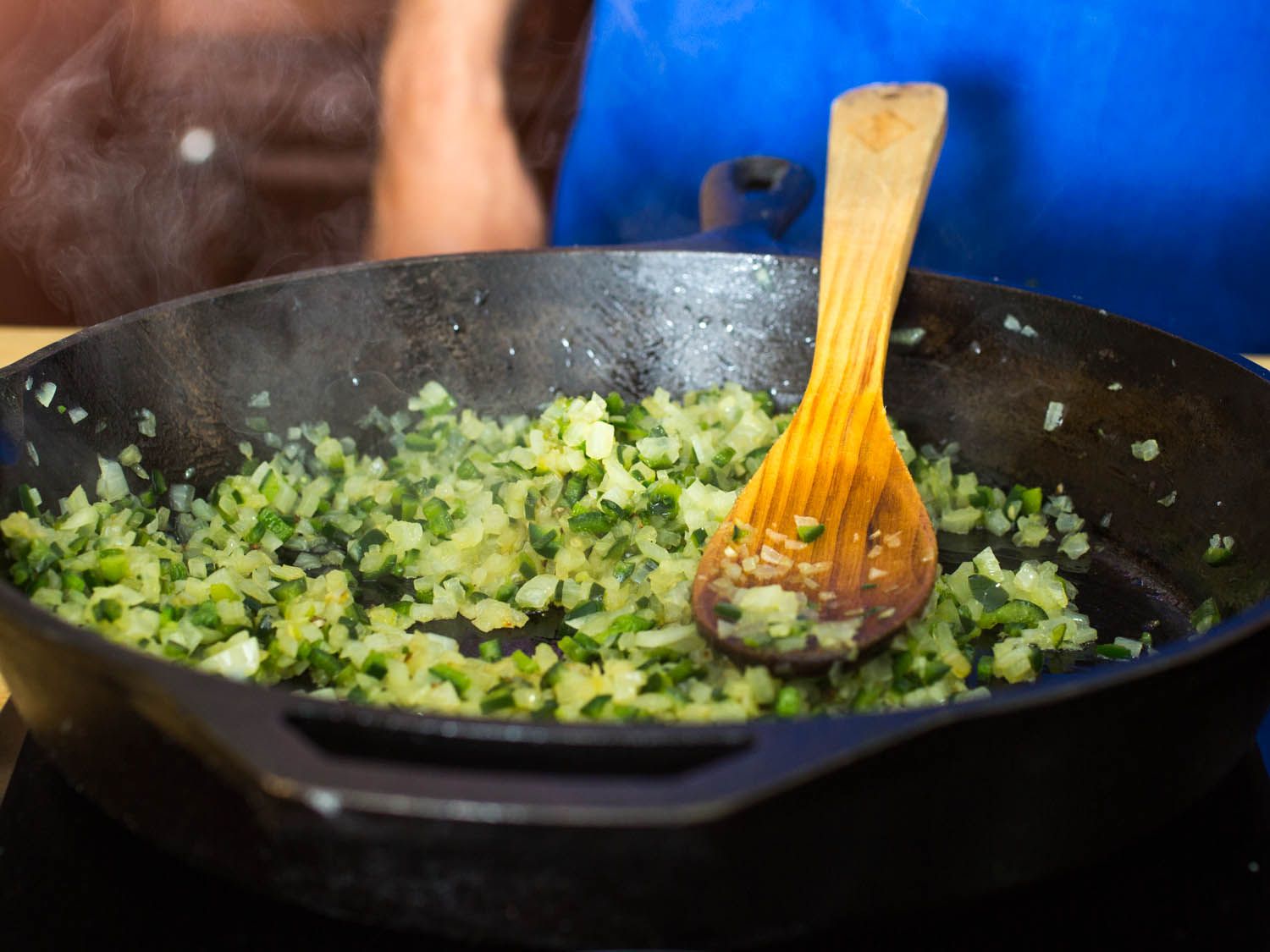 Stirring all of the diced chiles and onions in a cast iron skillet with a wooden spoon.