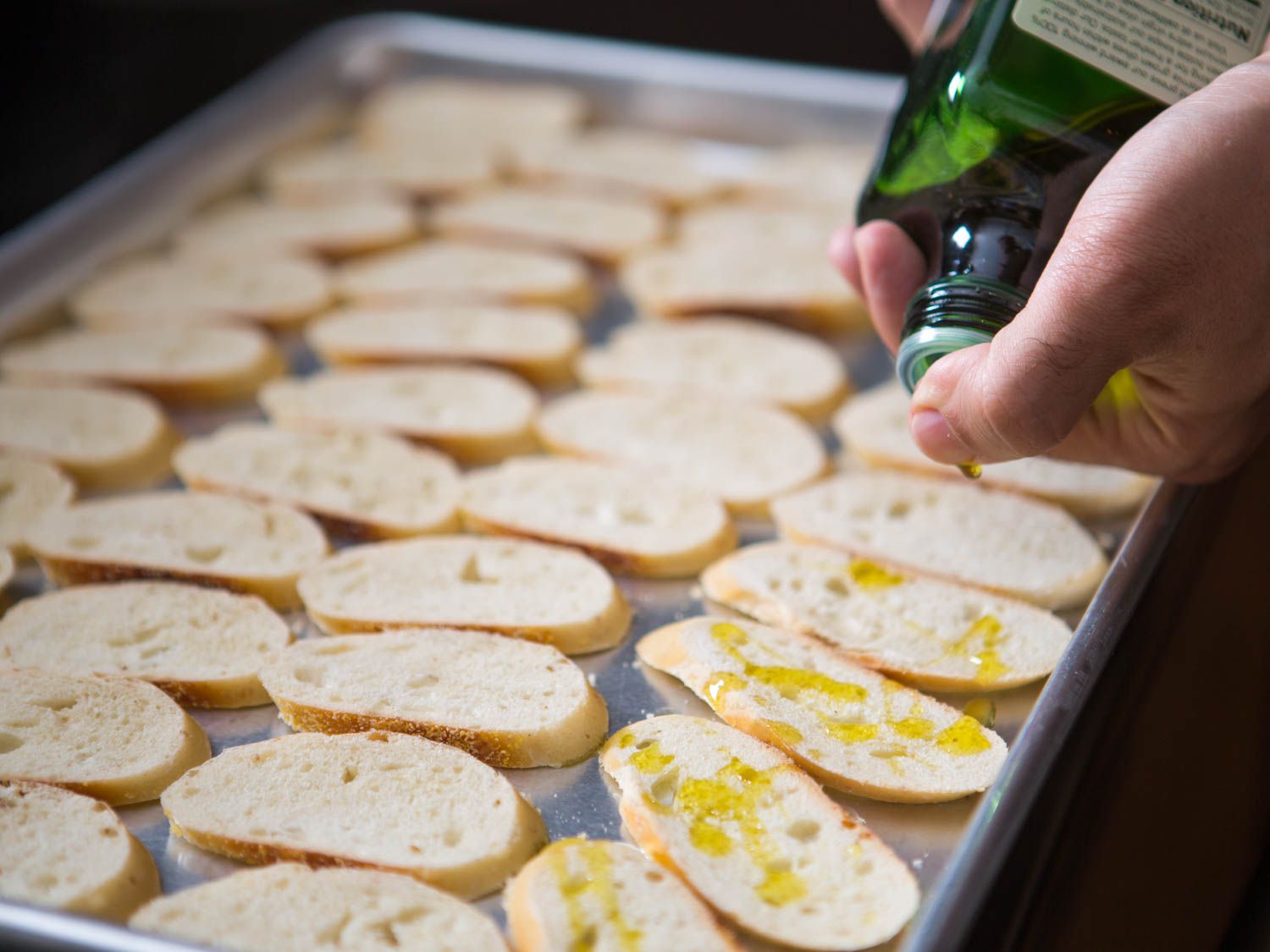 Drizzling olive oil over baguette slices to make baguette toast crackers