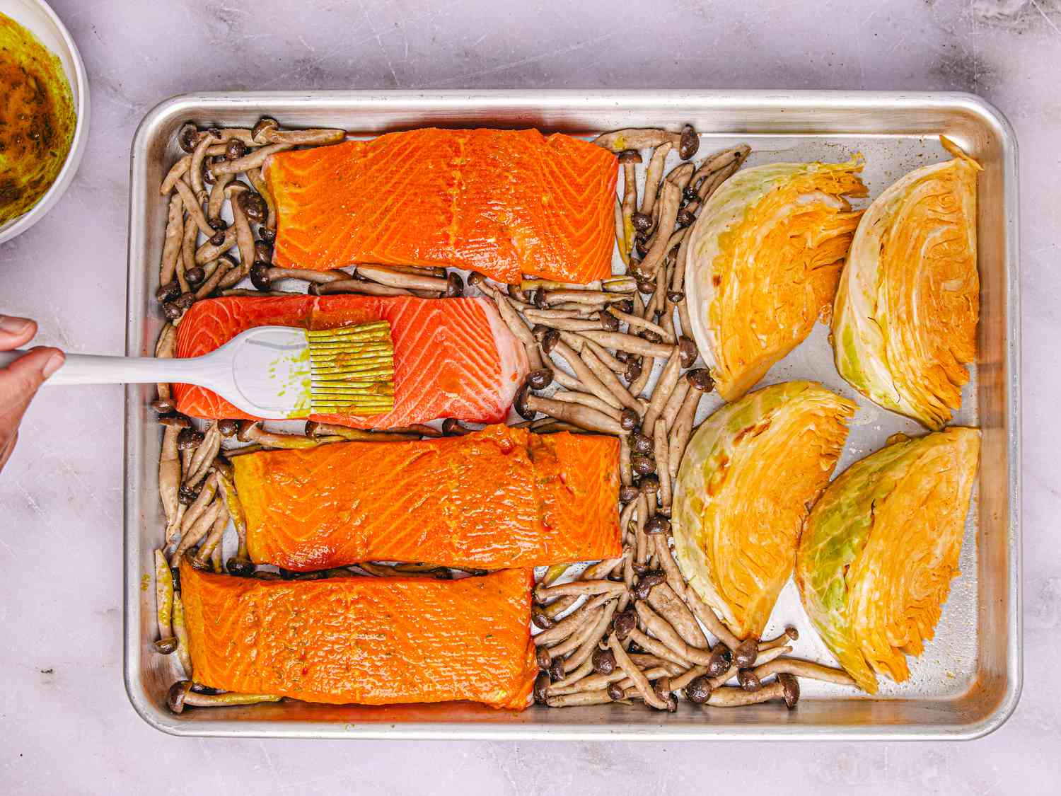 Salmon filets and vegetables on a baking sheet being brushed with sauce