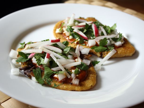 Huaraches with Black Beans and Radishes on a white plate.