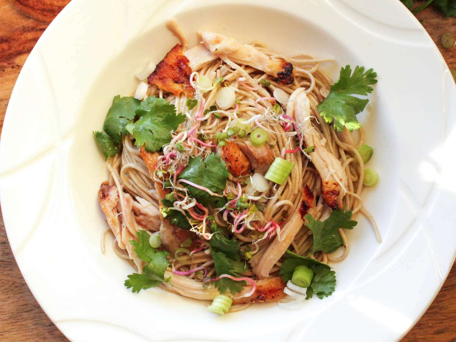 Overhead shot of a bowl of soba noodles in miso butter sauce, topped with shredded chicken, chopped scallion, and cilantro leaves.