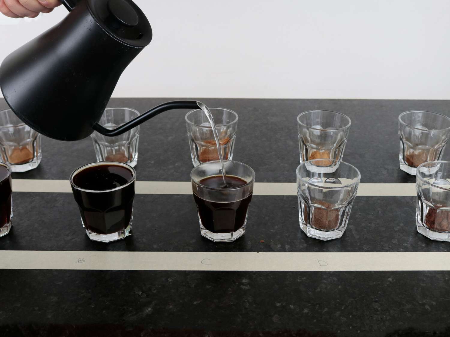 a gooseneck kettle pouring water into glass that contain instant coffee powder