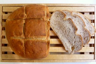 A boule of homemade bread on a wood slat board with three slices next to it. 