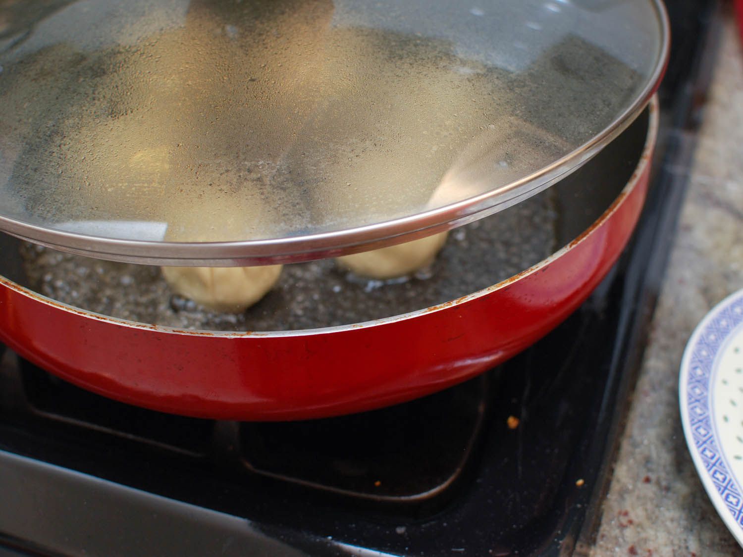 The skillet of cooking sheng jian bao is covered so that the dumplings can steam.