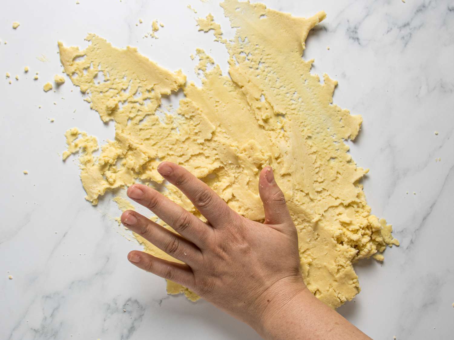 Hands smearing and mixing the dough together on a marble countertop 