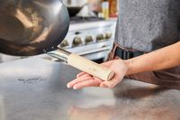 Person holding the handle of a Mammafong Pre-Seasoned Blue Carbon Steel Flat-Bottom Pow Wok