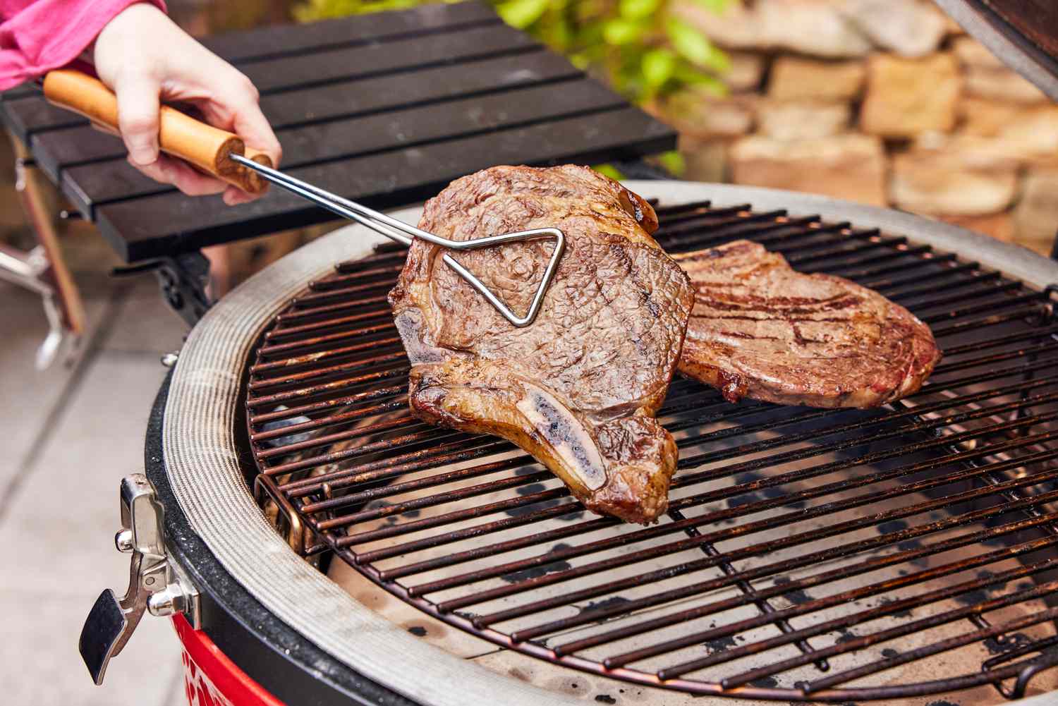 A person turns meat cooking in the Kamado Joe Classic II Charcoal Grill