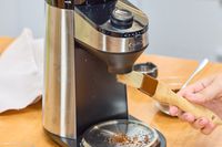 A person brushes the OXO Brew Conical Burr Coffee Grinder With Integrated Scale with a small brush