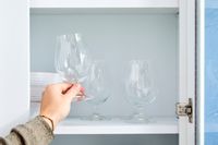 A person placing a tulip glass onto a kitchen shelf.