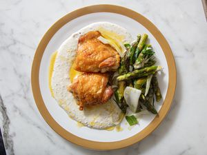 A plated dish with roasted chicken thighs, asparagus, and a creamy sauce