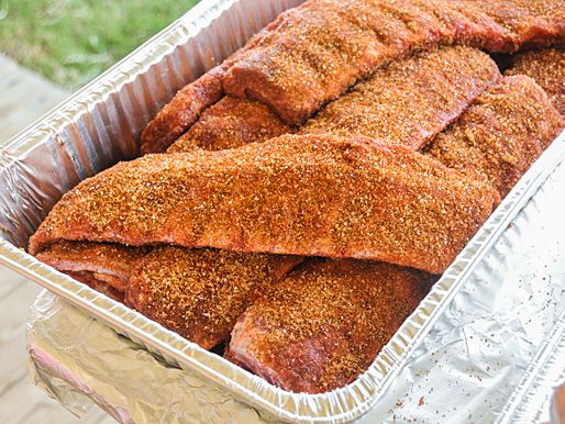 A disposable aluminum tray holding rub-coated, uncooked racks of pork ribs.