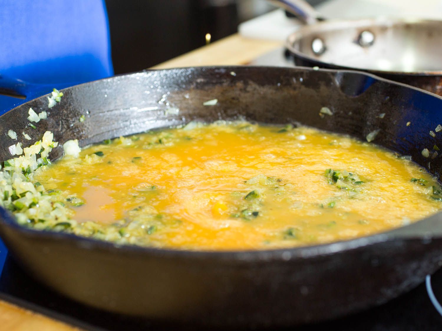 Uncooked eggs and vegetables combined in a cast iron skillet.