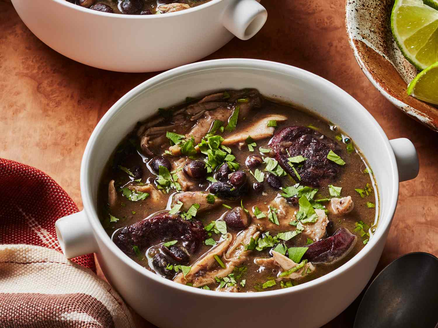 2 mugs of chicken and black bean soup with a bowl of limes on the side. 
