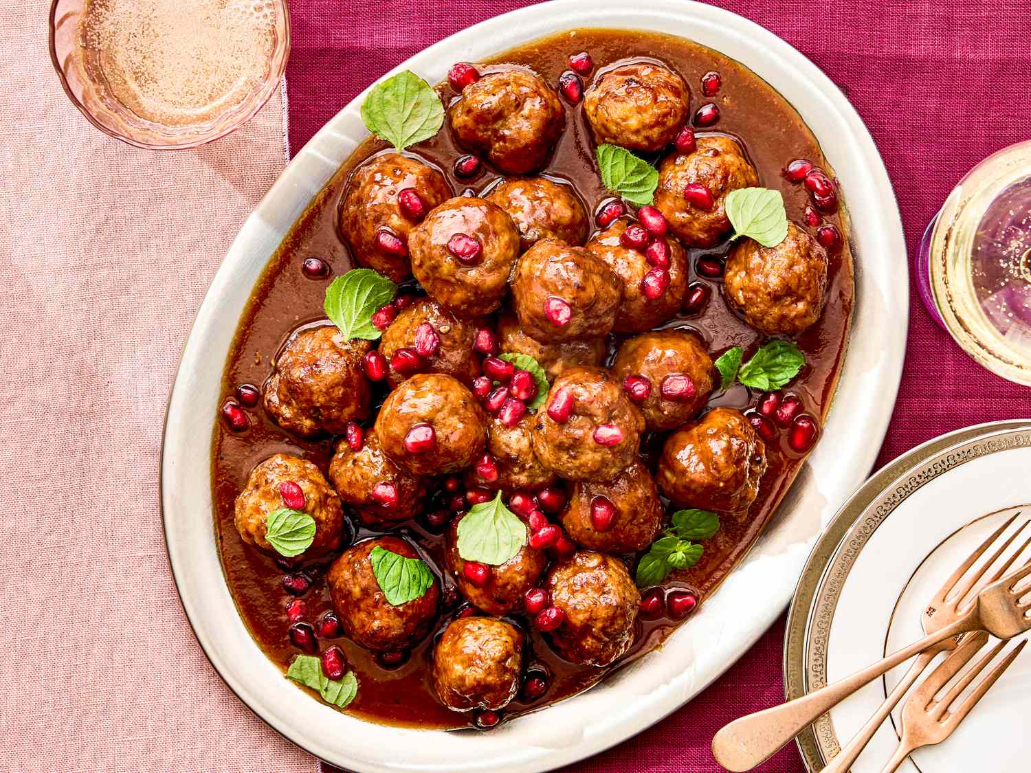 Plate of meatballs garnished with mint leaves and pomegranate seeds next to tableware