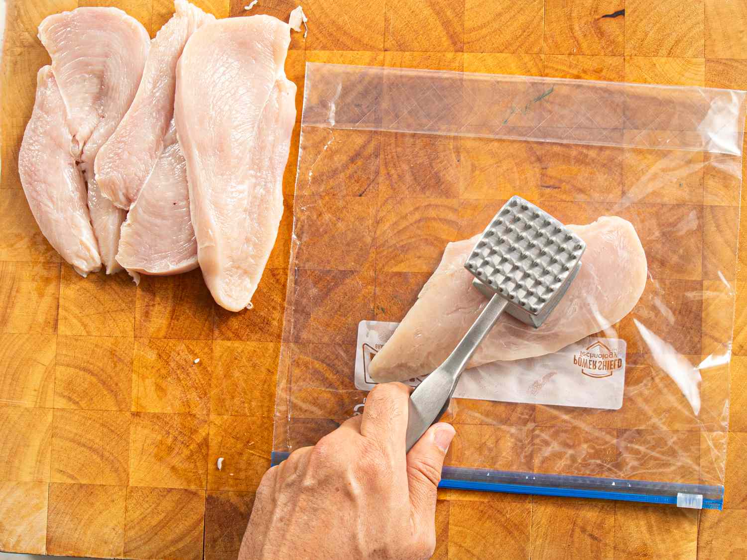 Overhead view of pounding a chicken breast with a mallet. 