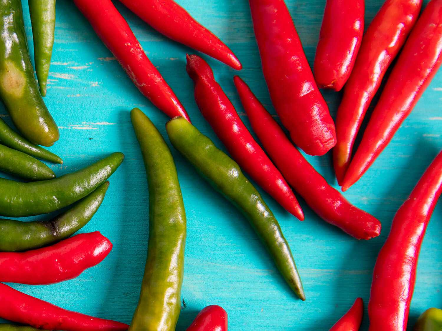 Red and green chile peppers on a blue surface.