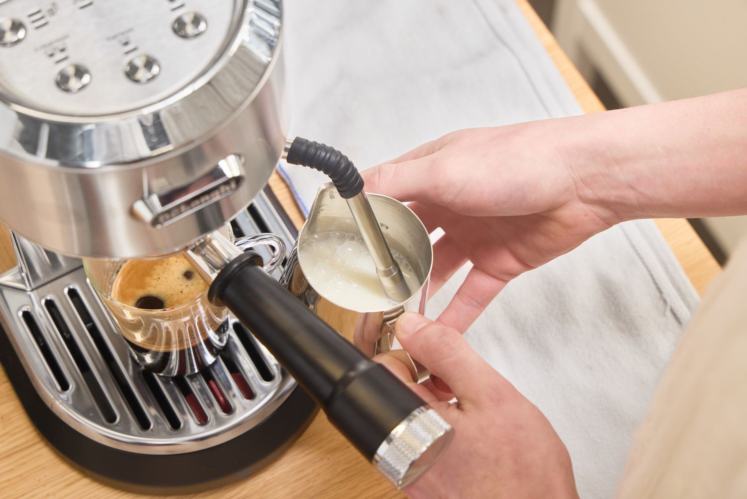 A person froths milk using the De'Longhi EC900M Dedica Maestro Espresso Machine