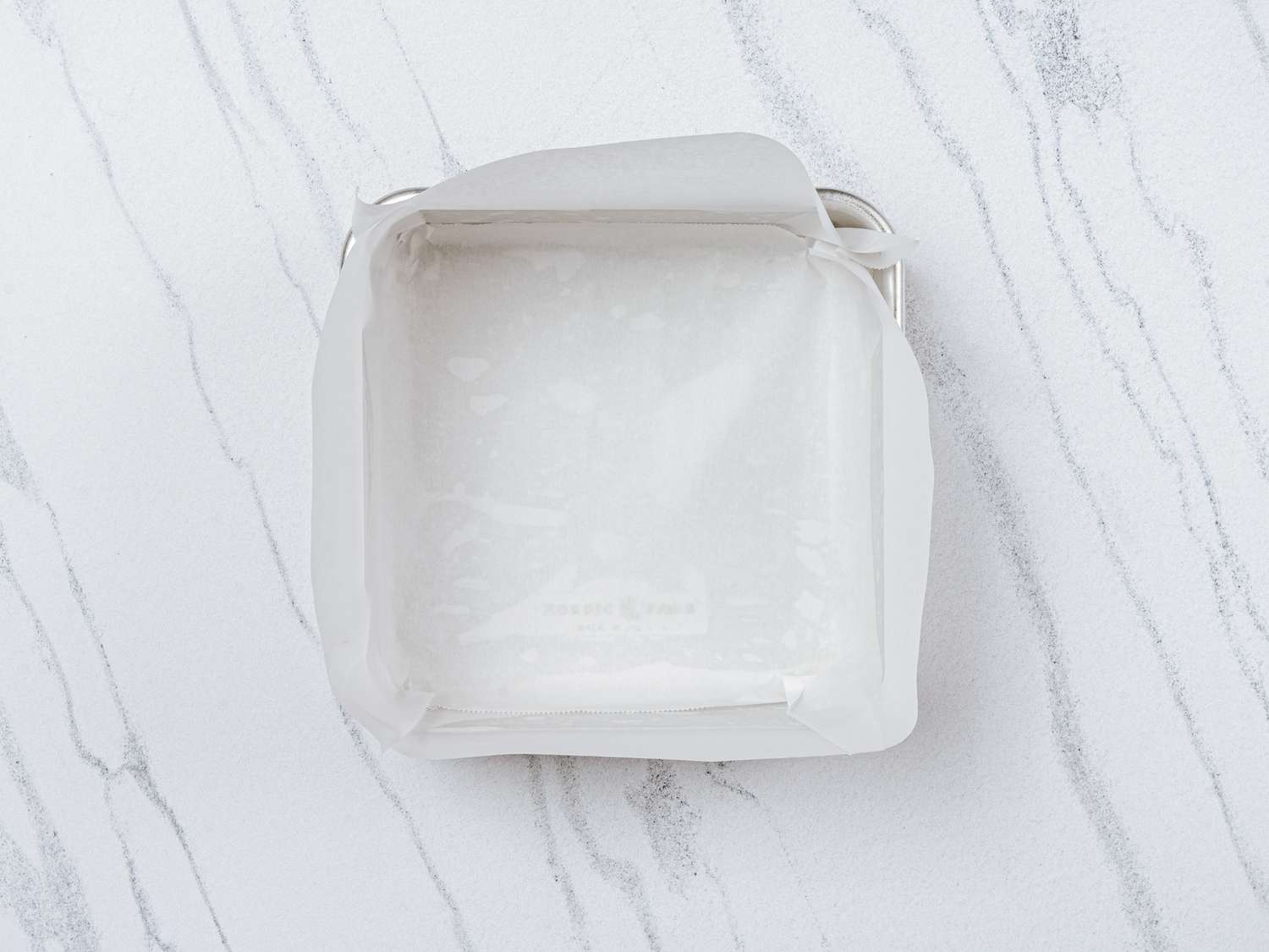 8x8 inch pan lined with strips of parchment paper on marble surface 