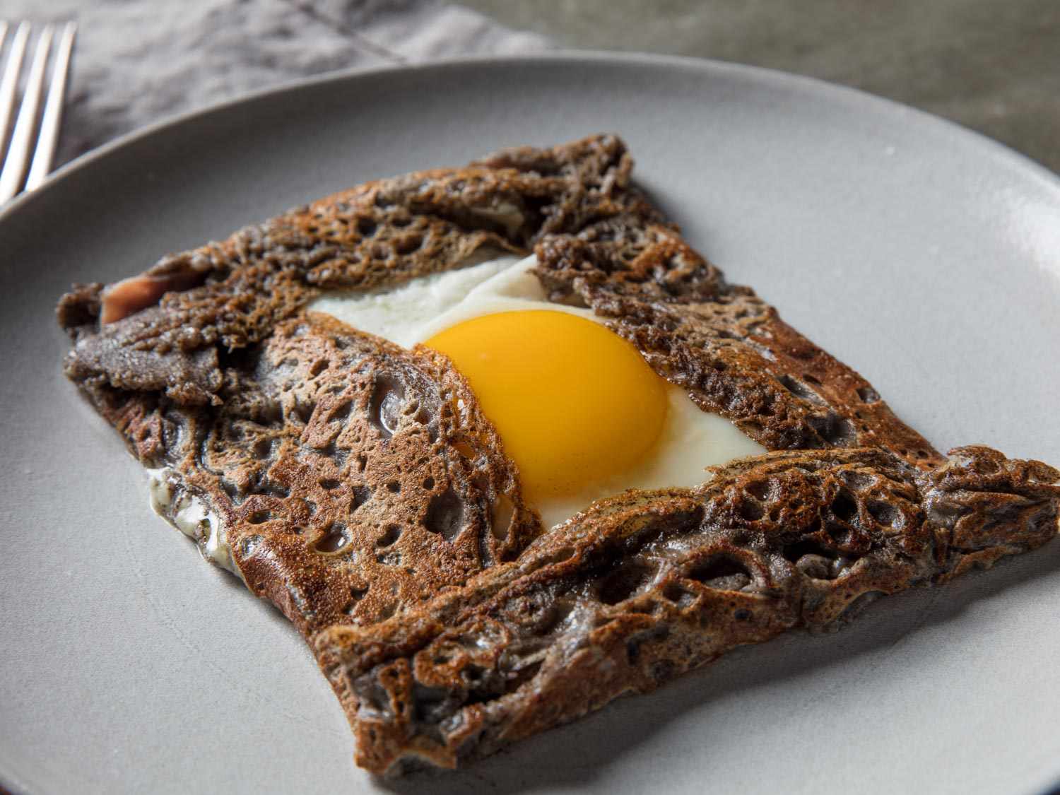 Close-up of a finished crepe on a grey plate with a sunny side egg peeking out.
