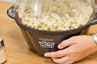 A person presses the power button on the West Bend Stir Crazy Electric Hot Oil Popcorn Popper