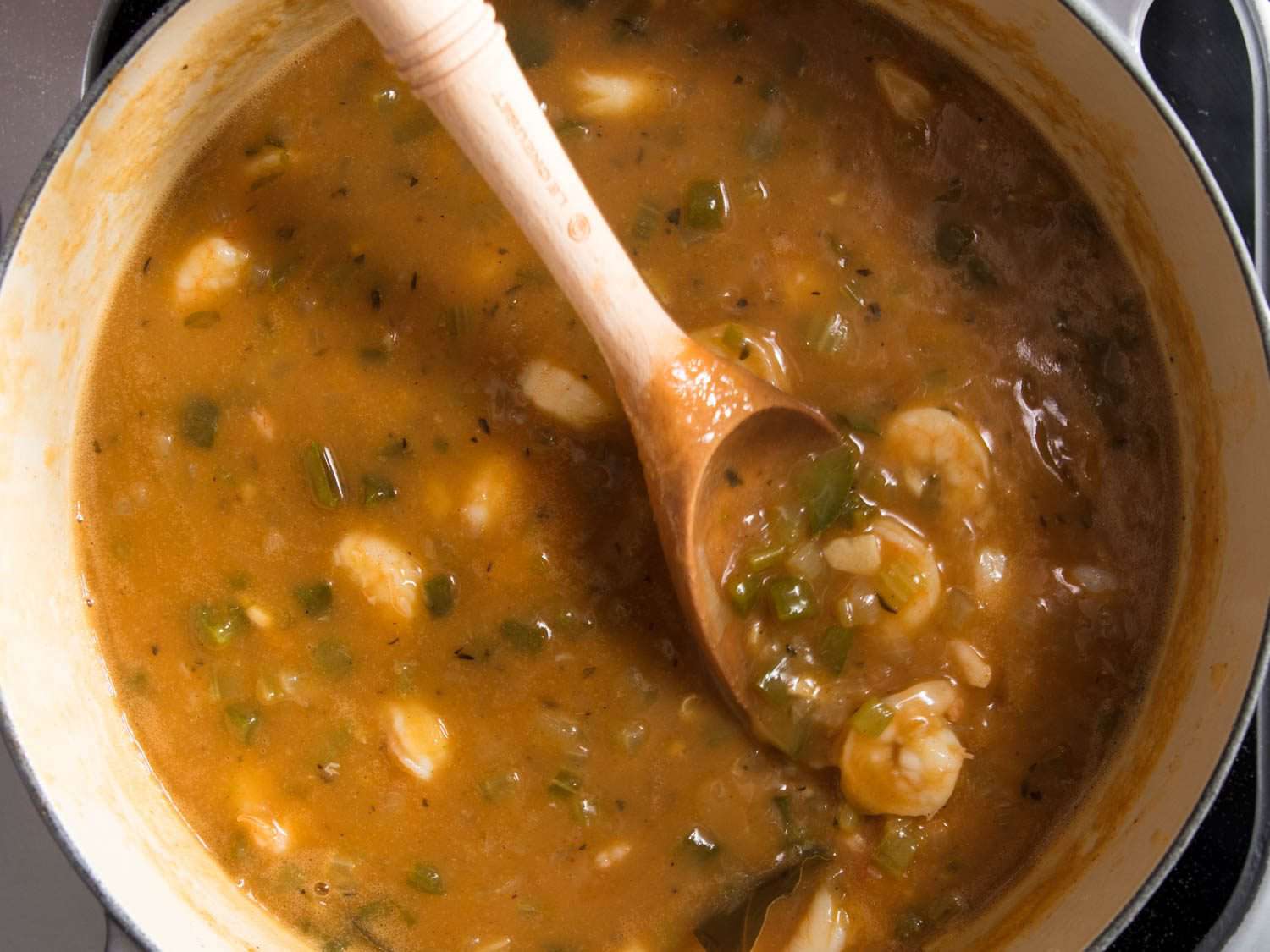 Shrimp etouffee made with a peanut butter roux in a pot, stirred with a wooden spoon.