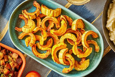 Roasted Delicata Squash on a turquoise platter, surrounded by thanksgiving dishes on a blue tablecloth