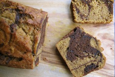 Overhead view of a loaf of marbled chocolate pumpkin bread being cut into slices.