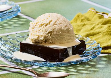 A dessert featuring a block of coffeeflavored gelatin topped with a scoop of ice cream and drizzled with cream on a glass plate
