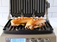 two cubano pressed sandwiches on a panini press with its lid upright