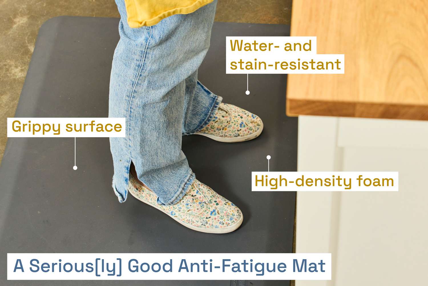 A person wearing jeans and sneakers standing on a black anti-fatigue mat