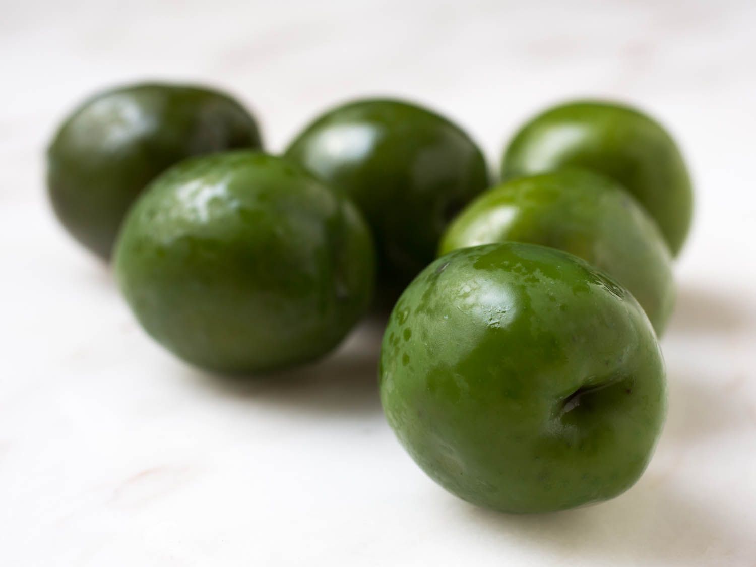 Closeup of small cluster of bright green olives on marble countertop