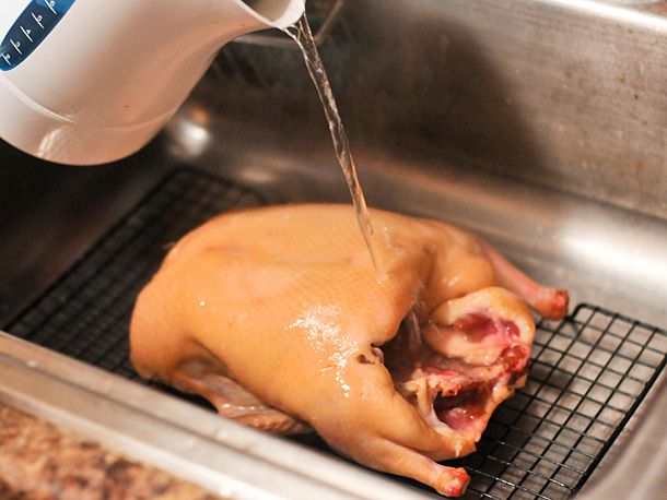 Pouring boiling water over the duck in a sink.