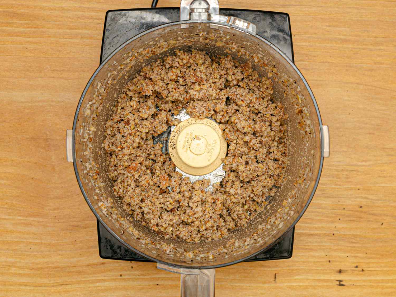 A food processor containing a walnut and skordalia mixture on a wooden surface