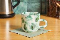 A green and white Ank Studios mug on a kitchen countertop.