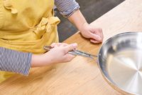 A person lifts the Tramontina 12-Inch Stainless Steel Skillet by the handle