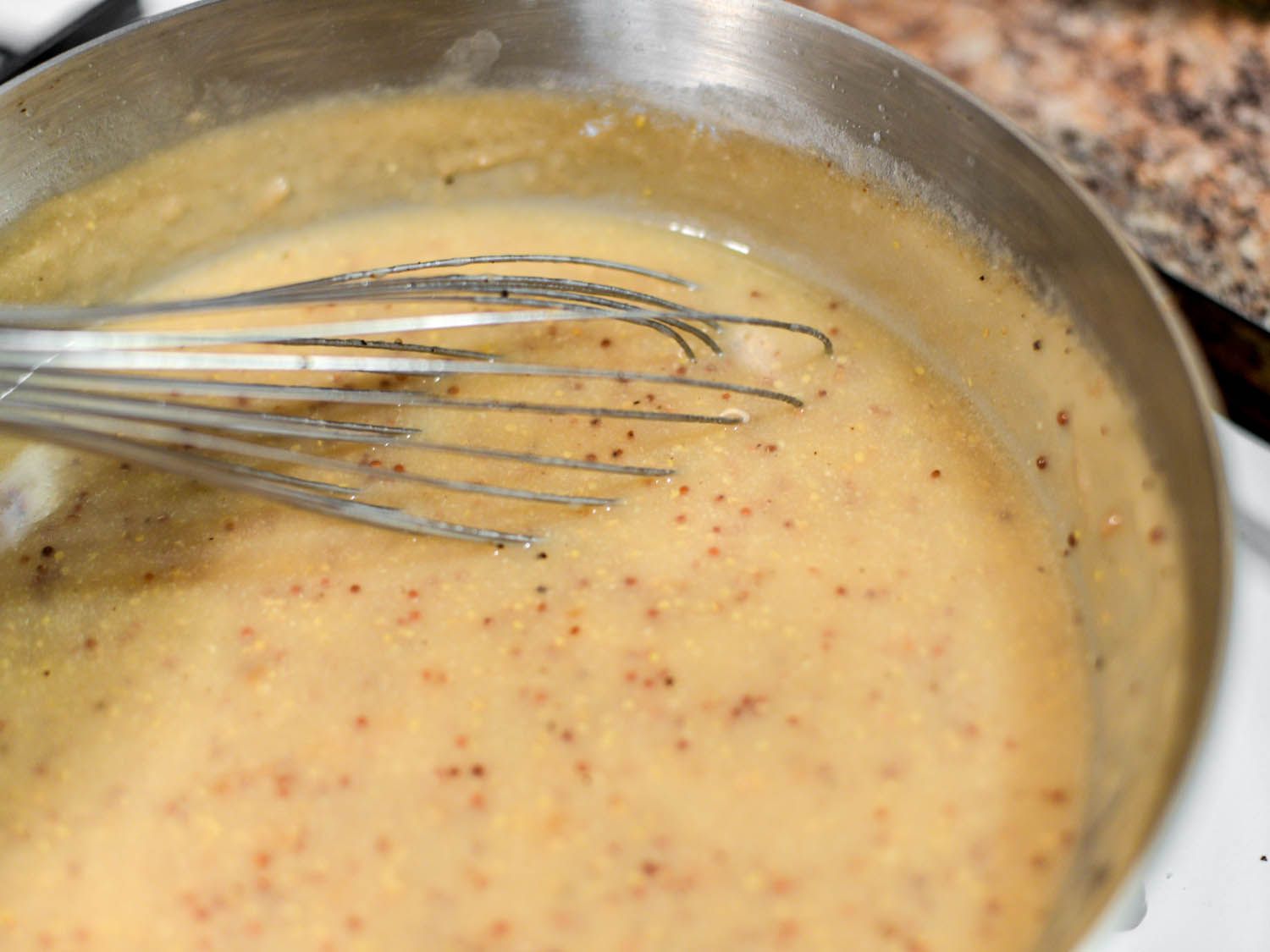 White wine and mustard gravy in a metal bowl being whisked.