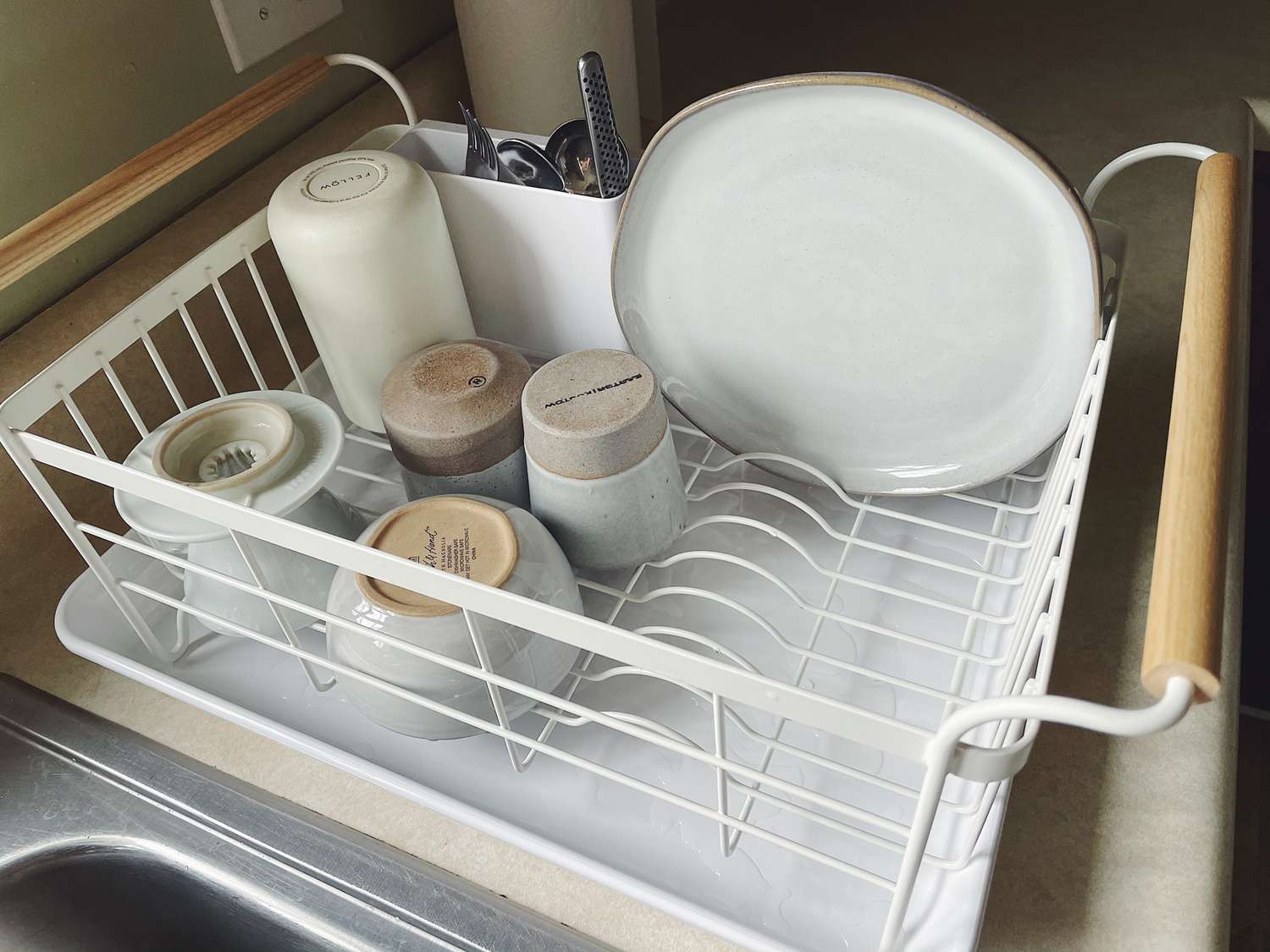 A white dish rack with wooden handles, filled with gray and white dishes.
