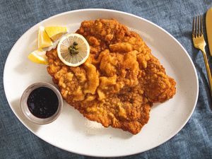 Plate of wienerschnitzel with lemon slices and dark sauce on the side