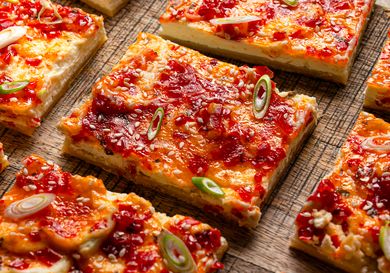 Cheese and pepper jelly tart slices garnished with sesame seeds and green onion pieces on a wooden surface