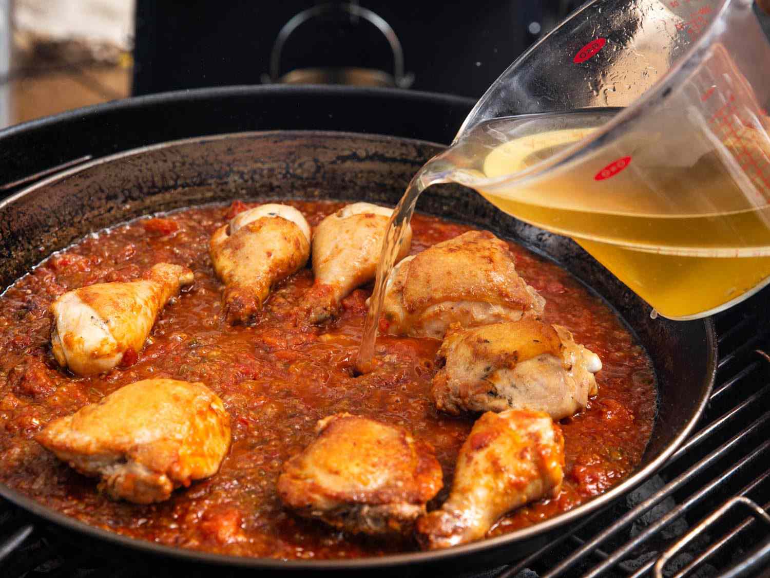 Adding stock to the paella pan after browning the proteins and aromatics.