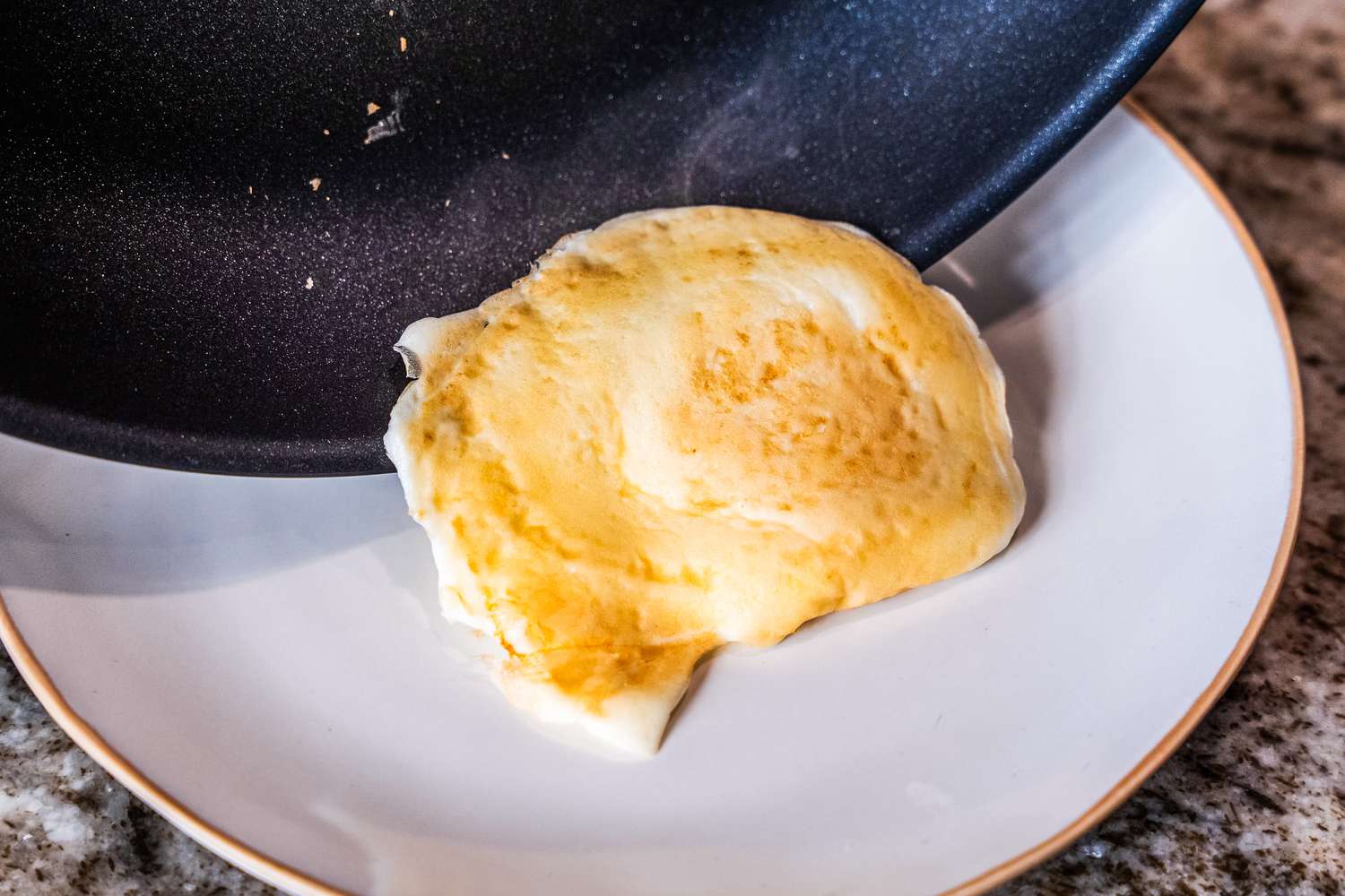 A fried egg is transferred from a black nonstick pan to a plate