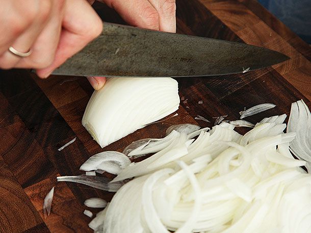 A knife about to slice into half of an onion. There is a large pile of sliced onions at the bottom of the image.