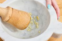 Garlic being crushed in a marble mortar and pestle.