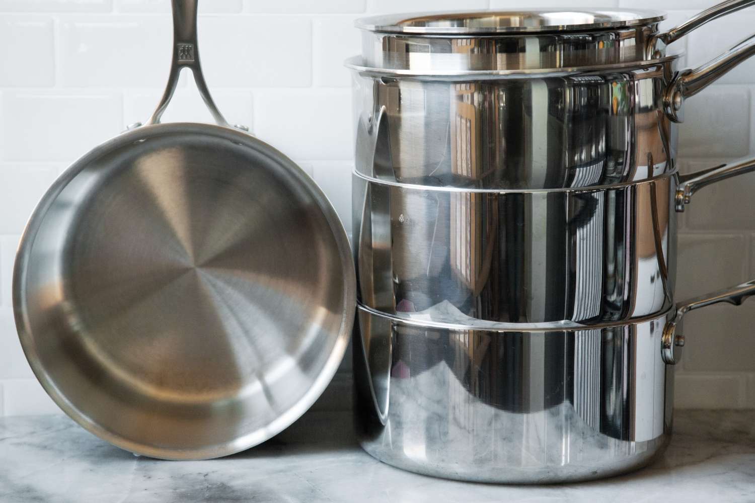 A stack of stainless steel pots and a frying pan resting on a countertop