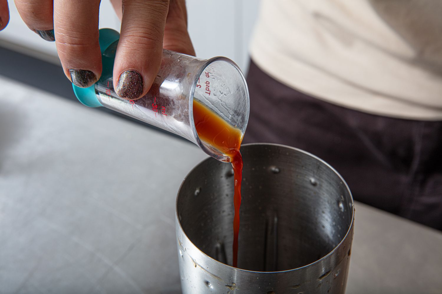 Hand pouring liquid from a measuring cup into a shaker