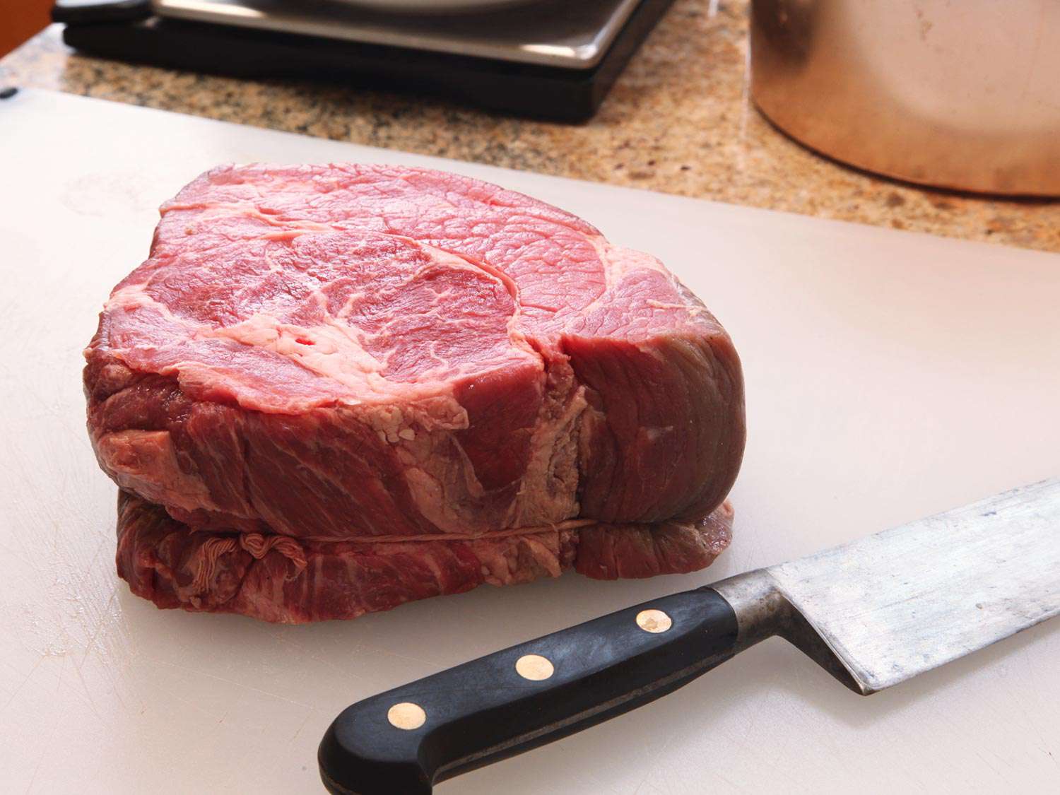 Beef chuck roast sitting on white cutting board next to chefs knife
